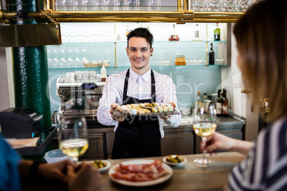 Young bartender serving food to customers at counter