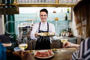 Young bartender serving food to customers at counter