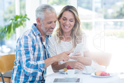 Mature couple looking in cellphone while sitting in restaurant