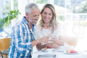 Mature couple looking in cellphone while sitting in restaurant