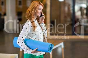 Smiling woman talking on phone while holding folded mat