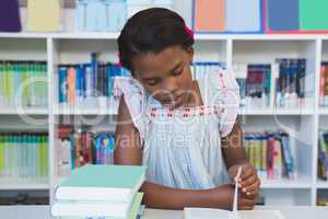 Schoolgirl sitting on table and reading book in library