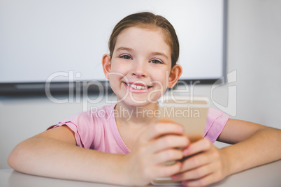 Smiling schoolgirl using mobile phone in classroom