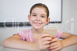 Smiling schoolgirl using mobile phone in classroom