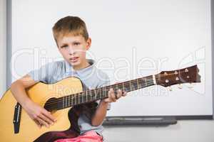 Portrait of schoolboy playing guitar in classroom
