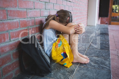 Sad schoolkid sitting alone in corridor