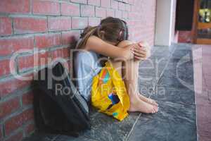 Sad schoolkid sitting alone in corridor