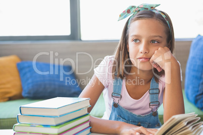 Schoolgirl sitting on table and reading book in library