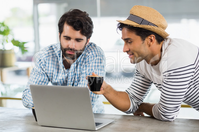 Two friends using laptop while having cup of coffee