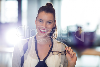 Portrait of woman holding eyeglass in office