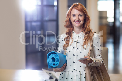 Portrait of woman holding mobile phone and folded mat