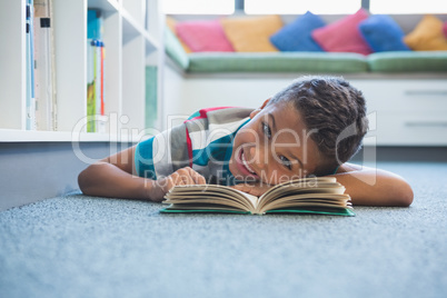 Schoolboy lying on floor and reading a book in library