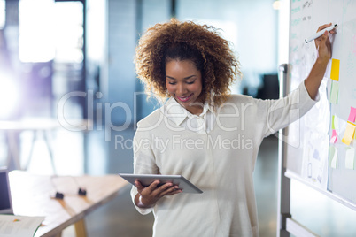 Woman writing on whiteboard while holding digital tablet