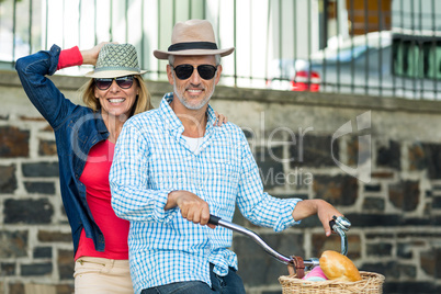 Portrait of happy mature couple riding bicycle against surrounding wall