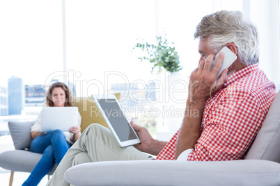 Side view of man talking on phone while holding tablet at home