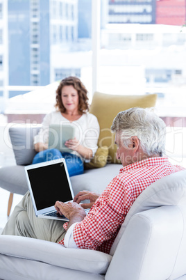 Mature man typing on laptop while sitting by woman