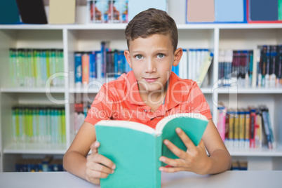 Schoolboy sitting on table and reading book in library