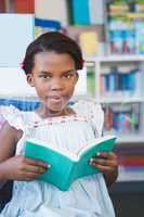 Schoolgirl sitting on chair and reading book in library