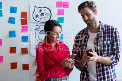 Young colleagues using mobile phones in creative office