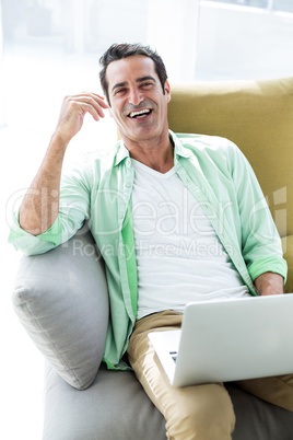 Happy man sitting with laptop on sofa