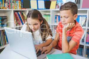 School kids using a laptop in library