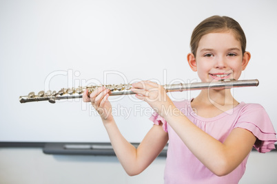 Portrait of smiling schoolgirl playing flute in classroom