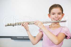 Portrait of smiling schoolgirl playing flute in classroom