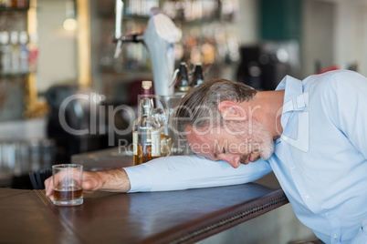 Unconscious businessman holding whiskey glass lying on a counter