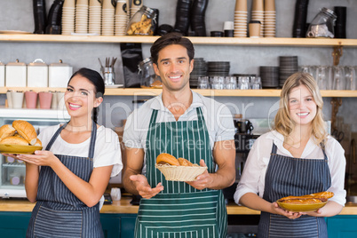 Smiling waiter and two waitresses holding plate of bread rolls