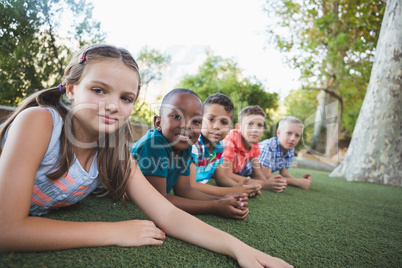 Smiling schoolkids lying on grass in campus