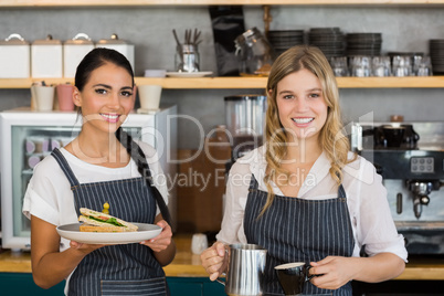 Portrait of two waitresses holding plate of meal and coffee jug