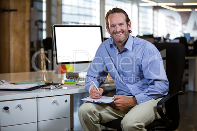 Businessman writing on clipboard by desk