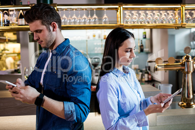 Man and woman using mobile phone by bar counter