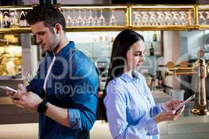 Man and woman using mobile phone by bar counter