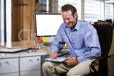 Businessman smiling while writing on clipboard