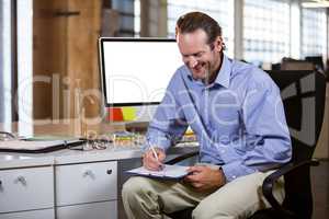 Businessman smiling while writing on clipboard