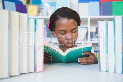 Schoolgirl sitting on table and reading book in library