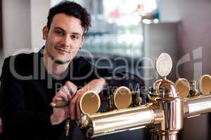 Handsome bartender leaning on beer tap
