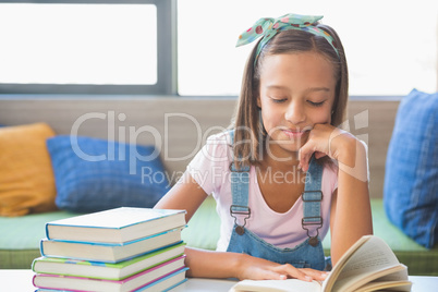 Schoolgirl sitting on table and reading book in library