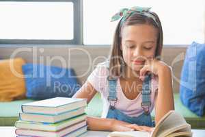 Schoolgirl sitting on table and reading book in library