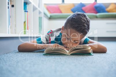 Schoolboy lying on floor and reading a book in library