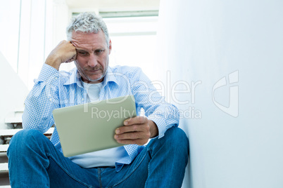 Tensed mature man holding tablet while sitting on steps