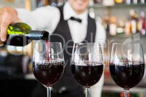 Waiter pouring wine into glasses