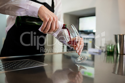 Bartender pouring wine in glass at bar counter