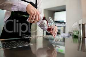 Bartender pouring wine in glass at bar counter