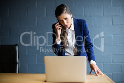 Woman talking on phone while using laptop in office