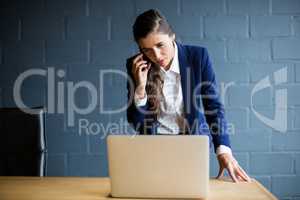 Woman talking on phone while using laptop in office