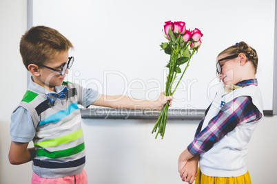 Schoolboy giving a bunch of flowers to a girl in classroom