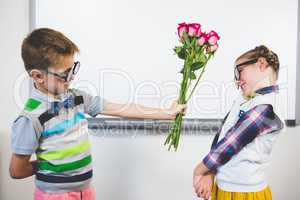 Schoolboy giving a bunch of flowers to a girl in classroom