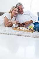 Smiling couple with red wine and food while lying on rug